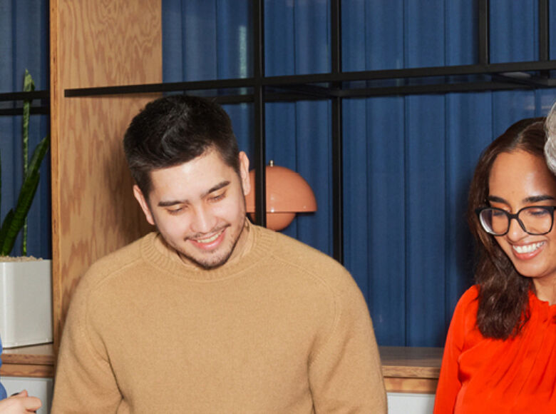 Vier Arbeitskolleg:innen unterhalten sich und lächeln dabei.